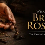 A broken wooden rosary and a frayed scapular resting on a dark wood table beside a glowing beeswax candle, illustrating how to dispose of blessed items.